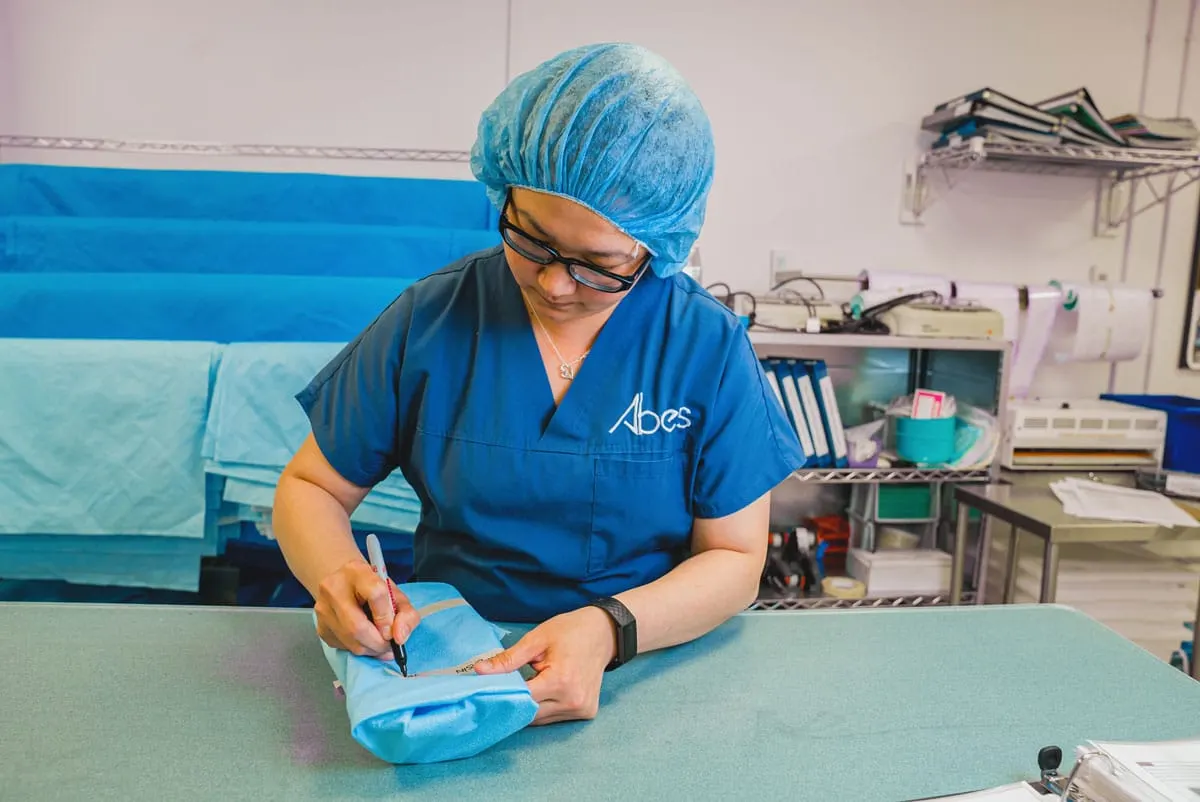 An ABES student in a surgical cap and scrubs wrapping a sterile instrument tray in the medical device reprocessing lab