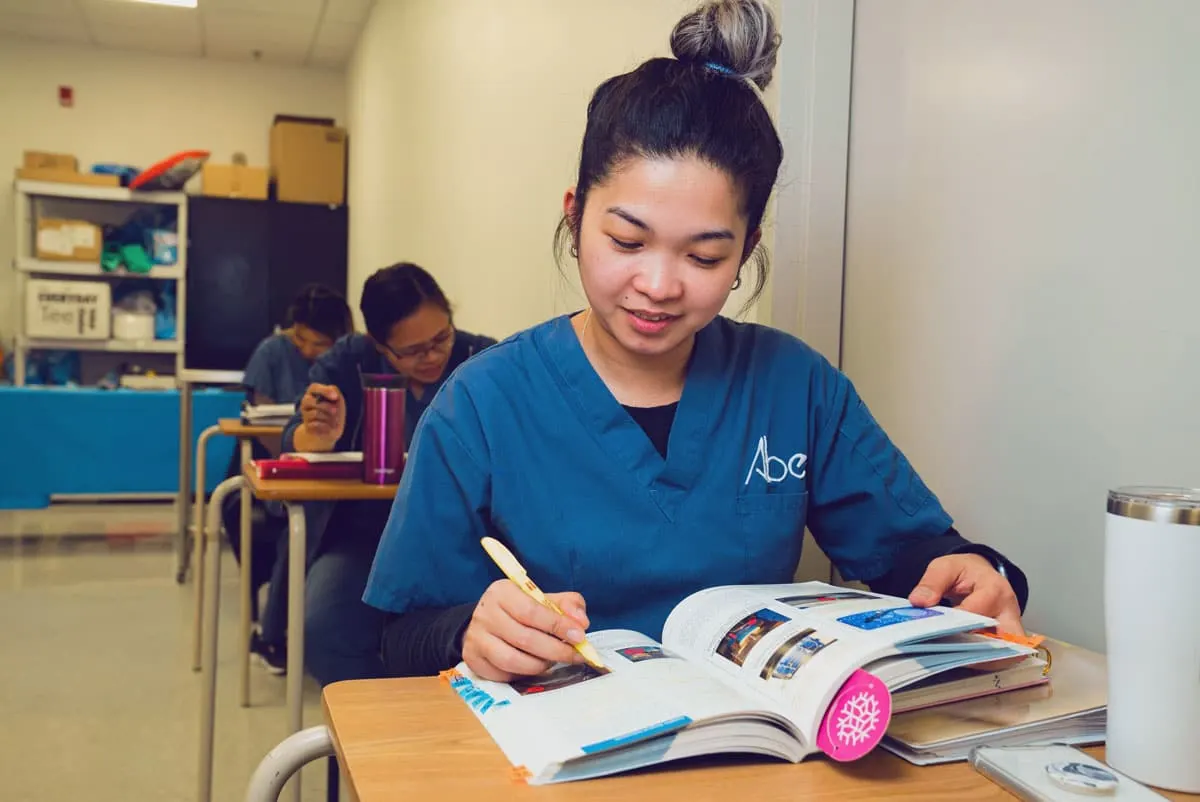 An ABES student in scrubs studying a textbook in class